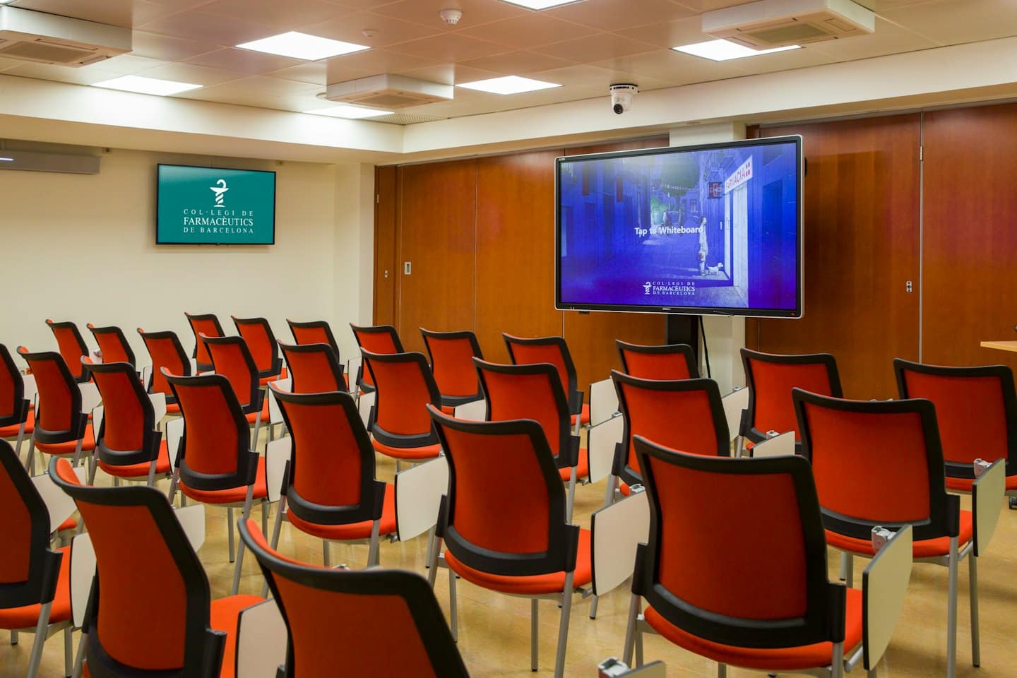 Moderna sala conferenze con sedie arancioni e grandi schermi per presentazioni.