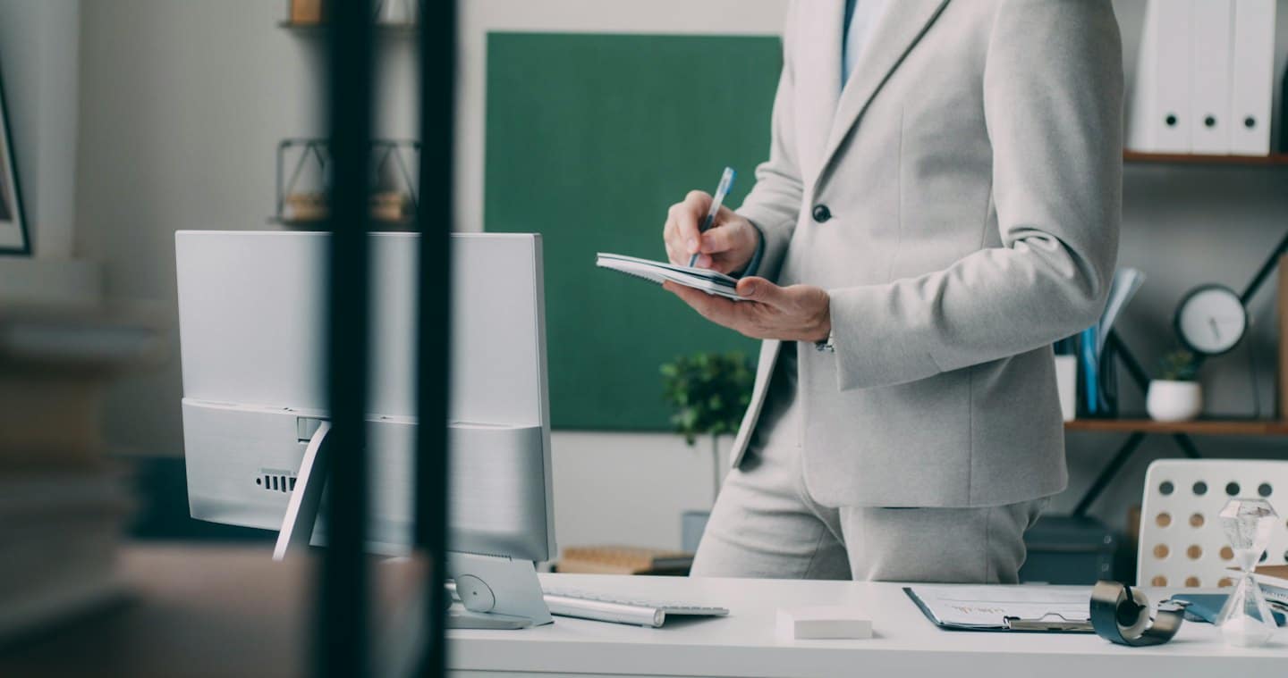Persona in abito grigio che prende appunti alla scrivania in ufficio.