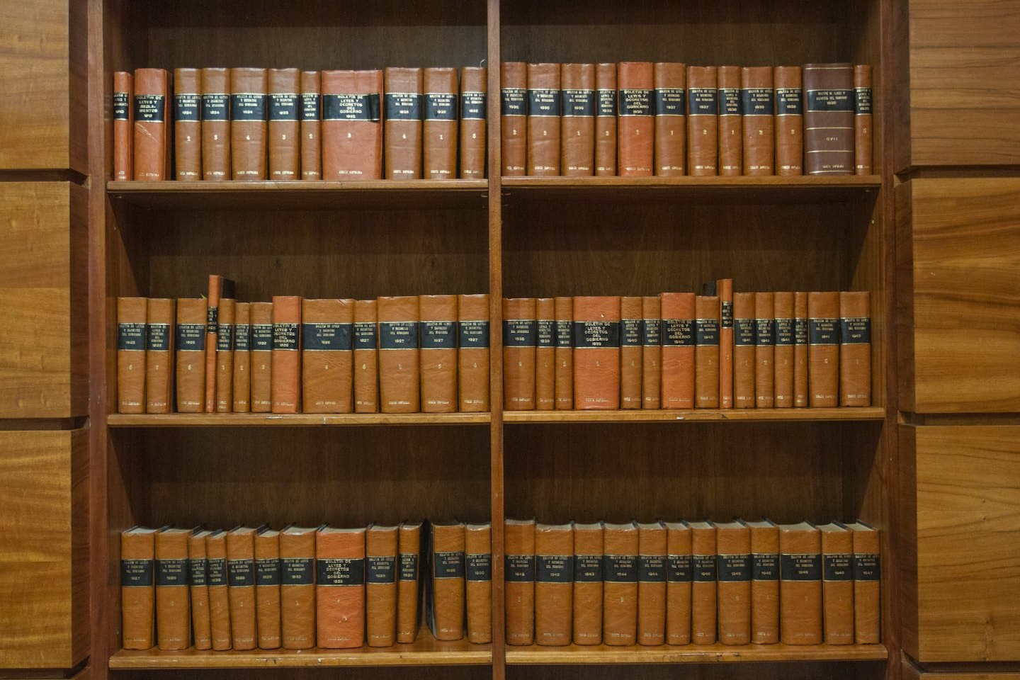 Vecchi libri di legge con copertine color cognac sono disposti su scaffali di legno.